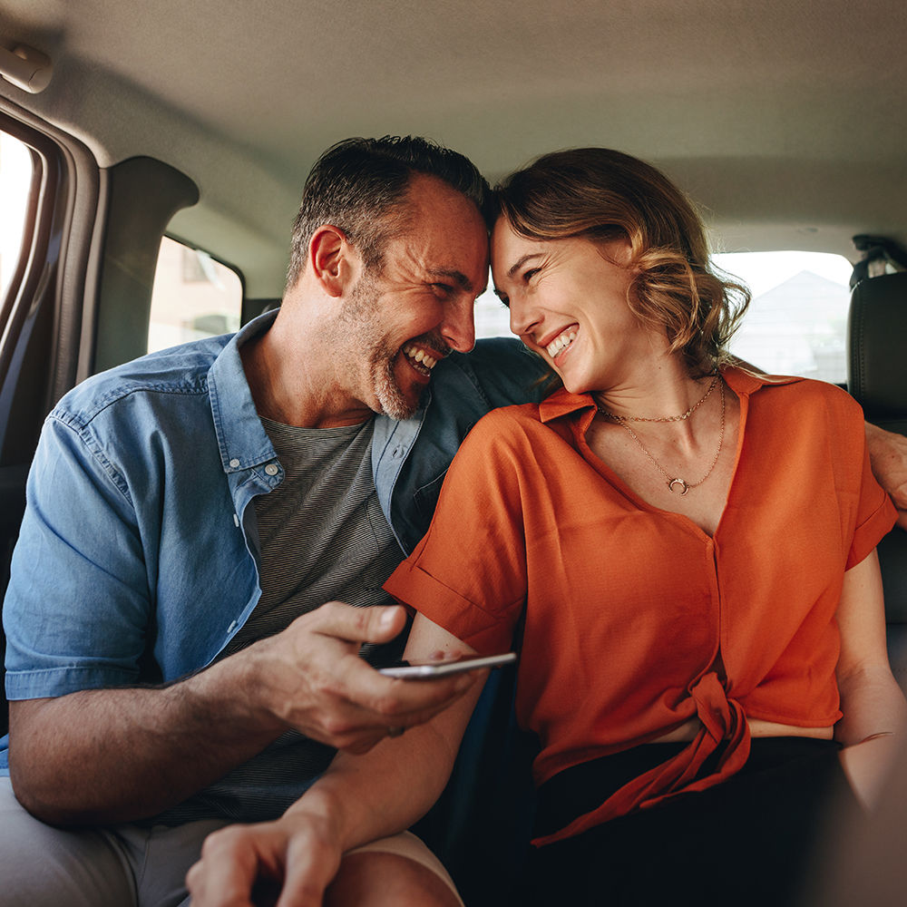 Happy couple smiling in the backseat of a car. Couple in love traveling by a taxi.